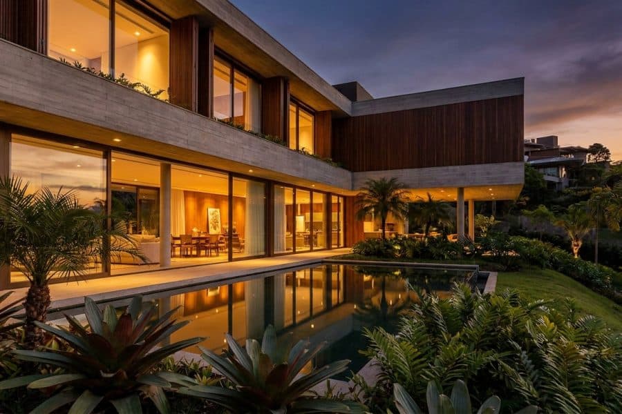 Fachada de casa de alto padrão contemporânea com grandes panos de vidro, iluminação quente e jardim integrado ao entardecer